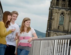 Drei Jugendliche stehen am Balkon. Im Hintergrund der Linzer Dom.