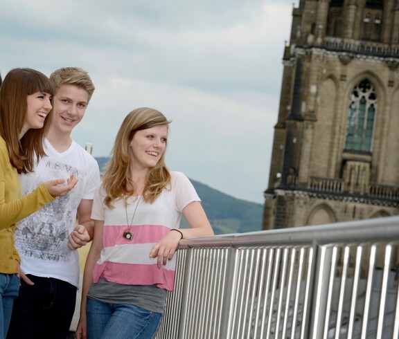 Drei Jugendliche stehen am Balkon. Im Hintergrund der Linzer Dom.