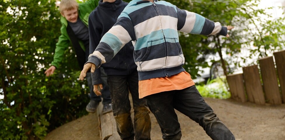 Drei Jungs balancieren über einen Holzbalken
