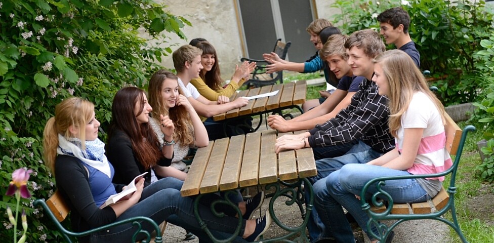 Mehrere Jugendliche sitzen draußen auf Tischen und unterhalten sich gut gelaunt.